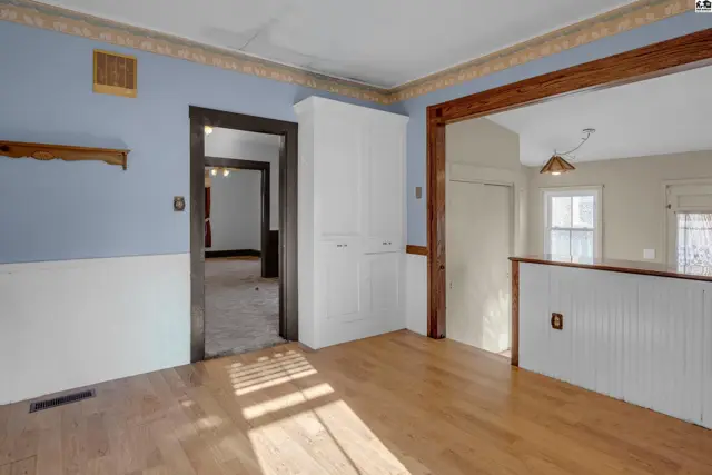 Light-filled dining area with blue walls, white wainscoting, and hardwood floors opening to another room.
