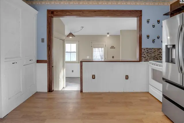 Bright kitchen with white cabinets, light wood floors, and a pass-through to a sunlit dining area.