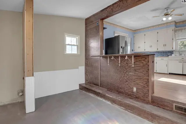 Interior view of a dining area with a wood-paneled bar opening to a kitchen with white cabinets.