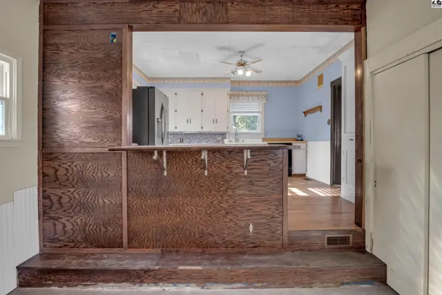 View into a kitchen with white cabinets and blue walls, framed by dark wood paneling.