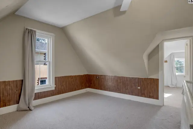 Attic bedroom with sloped ceiling, wood paneled wainscoting, and neutral carpet.