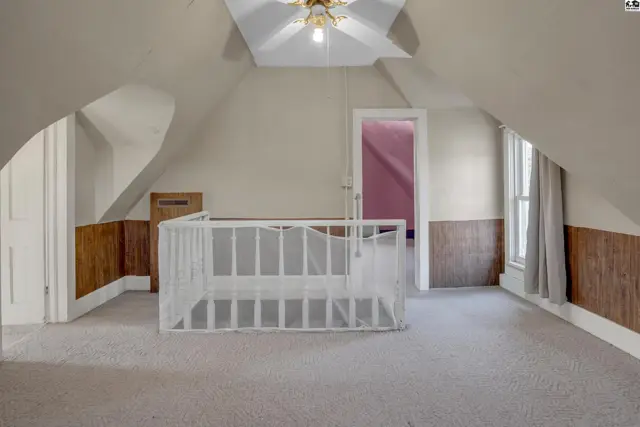 Attic room with sloped ceilings, carpet, wood paneling, and a white railing.