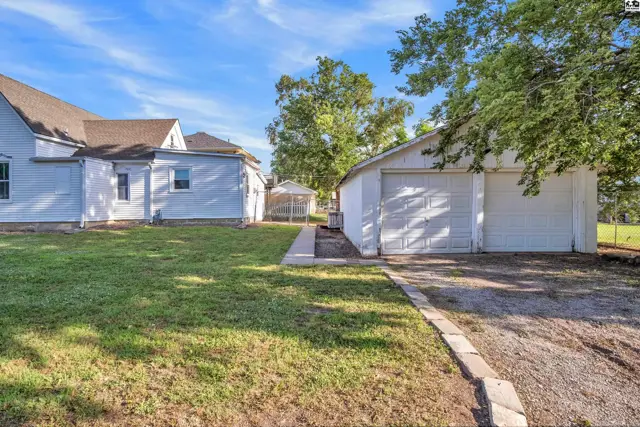 White siding house with a two-car garage and gravel driveway on a sunny day.