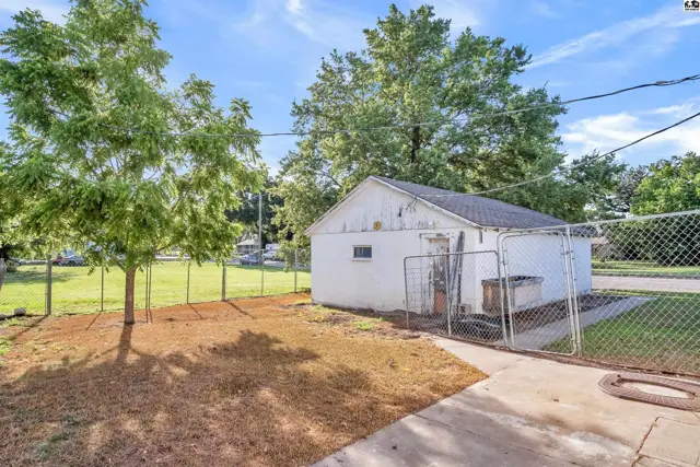 White detached garage with a chain-link fence and mature trees in a sunny backyard.