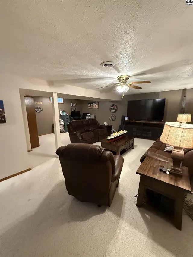 Spacious living room with plush brown leather furniture, a large television, and a ceiling fan.