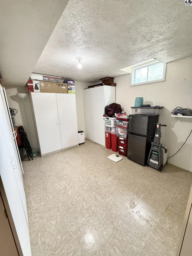 Unfinished basement with storage cabinets, a mini-fridge, and a vacuum cleaner.