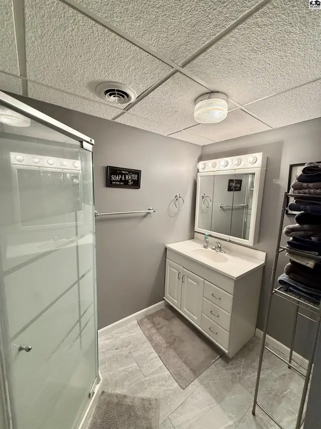 Modern bathroom with a glass-enclosed shower, white vanity, and tiled floor.