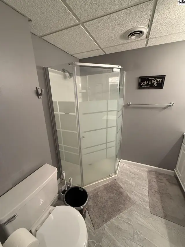Modern bathroom features a glass-enclosed shower, gray walls, and tiled flooring.