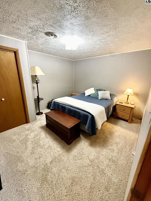 Cozy bedroom with plush carpet, a wooden chest, and a queen-size bed with blue bedding.