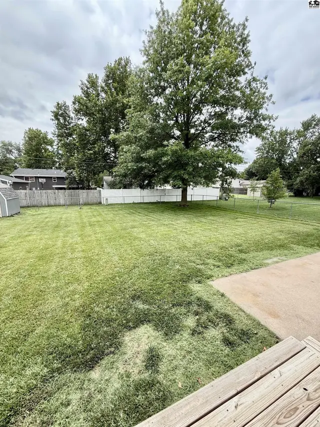 Spacious, level backyard with mature trees, white vinyl fencing, and a concrete patio.