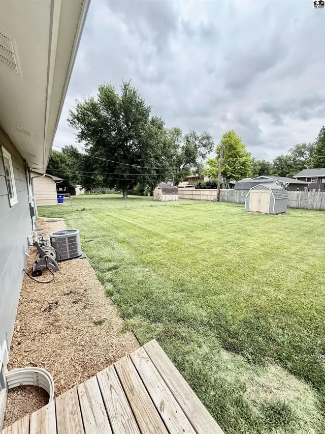 Spacious, level backyard with mature trees, a wooden deck, and two storage sheds.