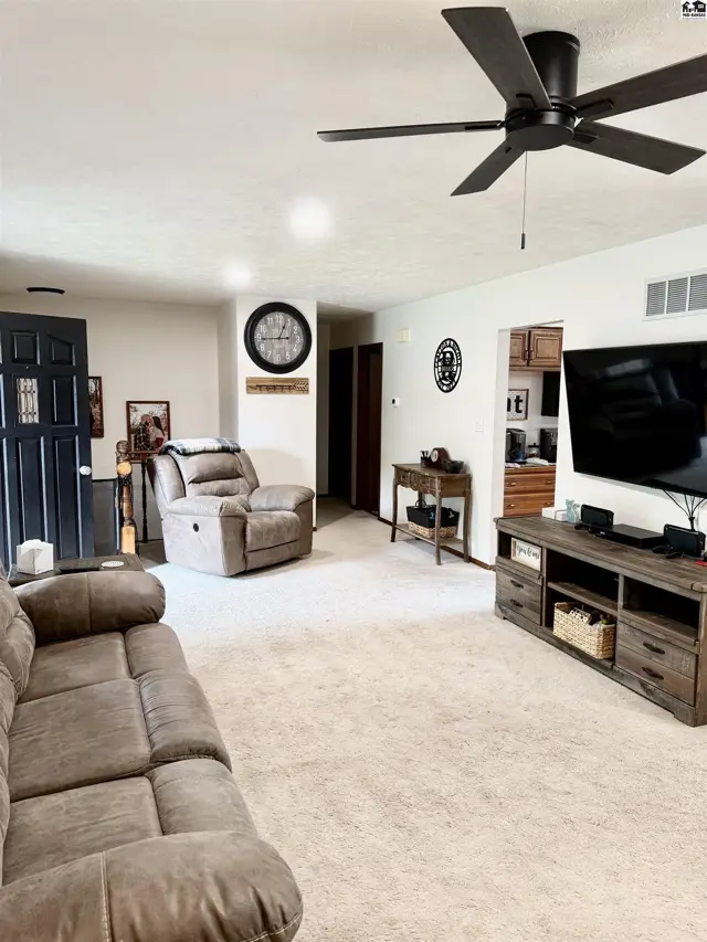 Cozy living room with plush taupe sofa, recliner, large TV, and ceiling fan.