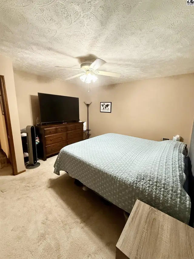 Spacious bedroom with a king-size bed, dresser, TV, and ceiling fan.