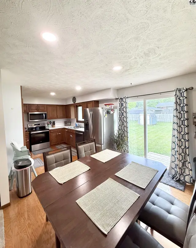 Dining area with upholstered chairs and a view of a modern kitchen and backyard.