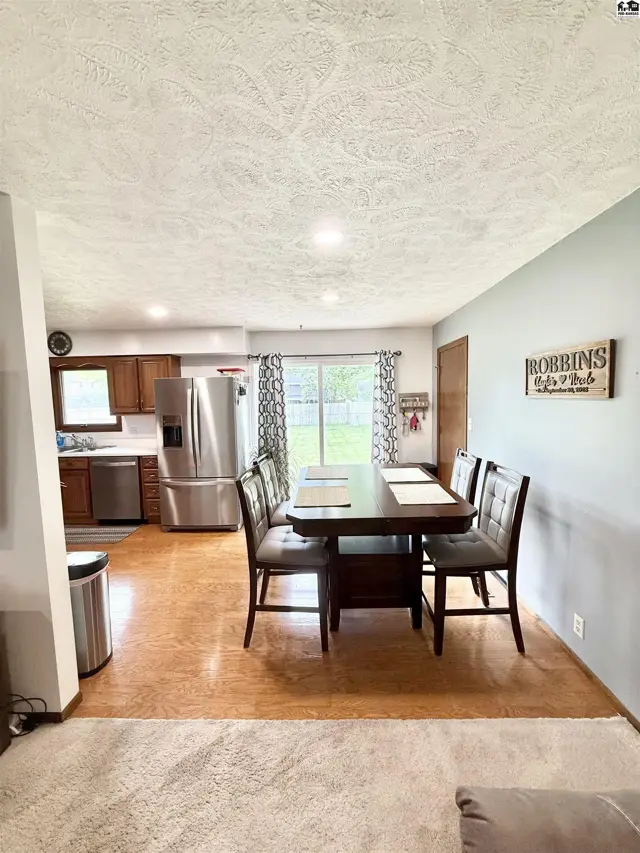 Dining area with dark wood table and upholstered chairs adjacent to a stainless steel kitchen.