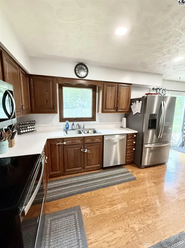 Spacious kitchen with dark wood cabinets, white countertops, stainless steel appliances, and light wood flooring.