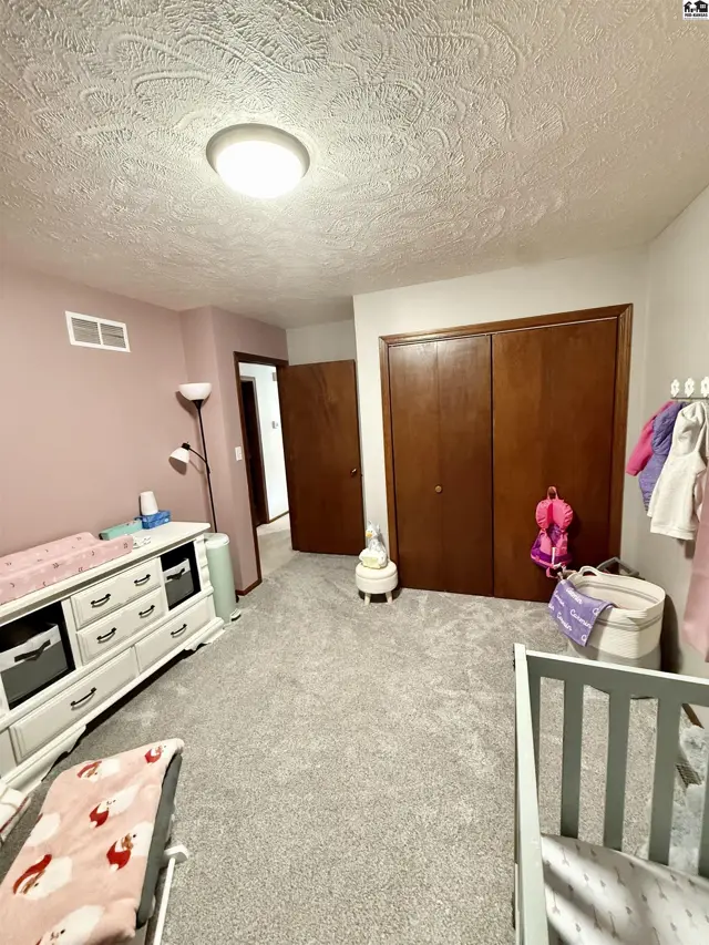 Nursery with white dresser, gray carpet, and wooden closets.