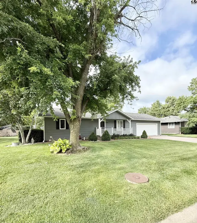 Gray ranch home with white trim, attached garage, and mature trees on a manicured lawn.