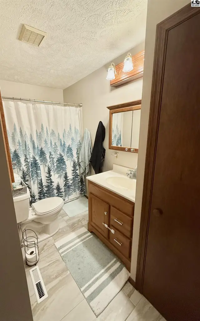 Bathroom with wood vanity, forest-themed shower curtain, and light gray tile flooring.