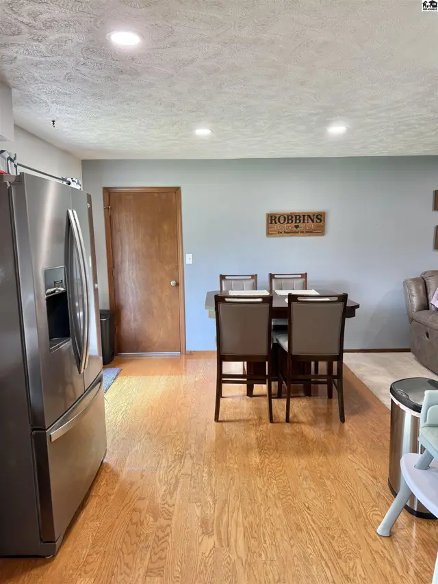 Open dining area with wood floors, stainless steel refrigerator, and a dark wood table with four chairs.