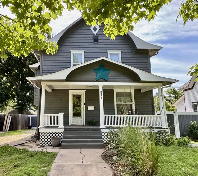 Gray clapboard house with a prominent teal star on the arched porch, white railings, and lattice.