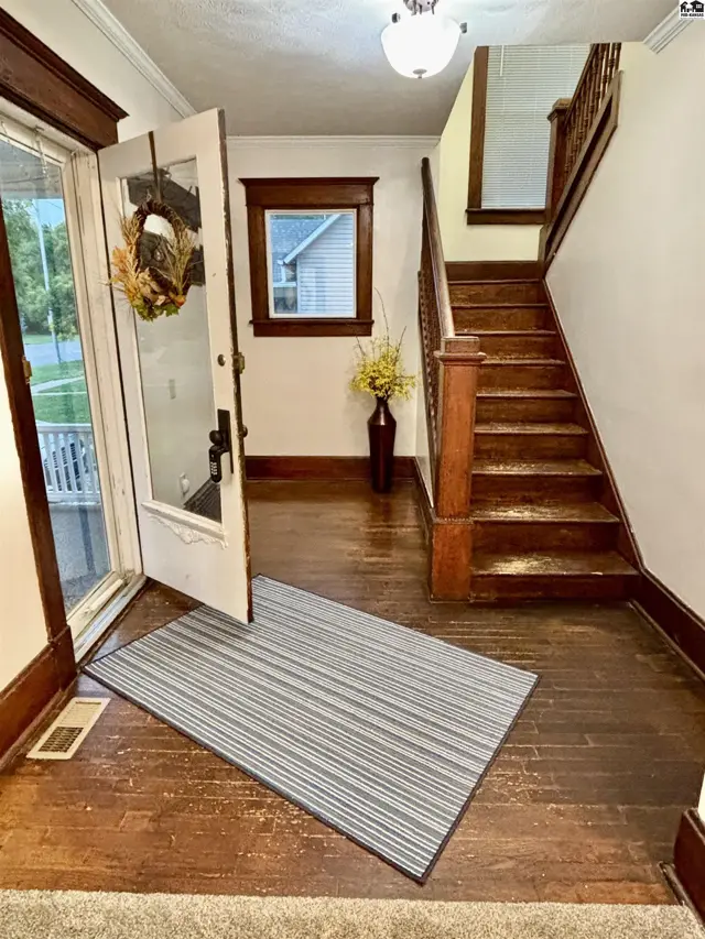 Warm entryway with dark wood floors, trim, and staircase, plus a glass-paned door.