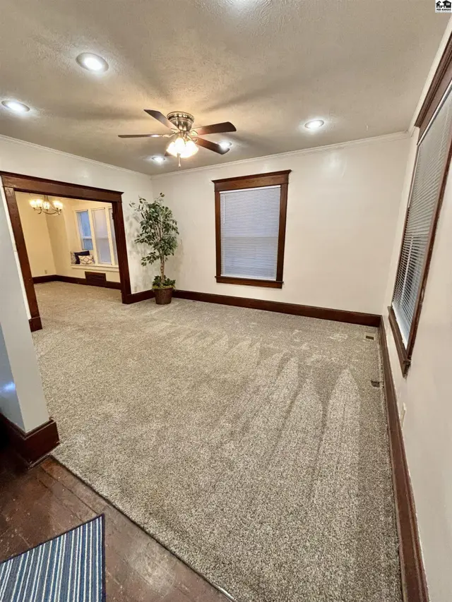 Spacious living room with plush carpet, dark wood trim, and a ceiling fan, opening to a dining area.
