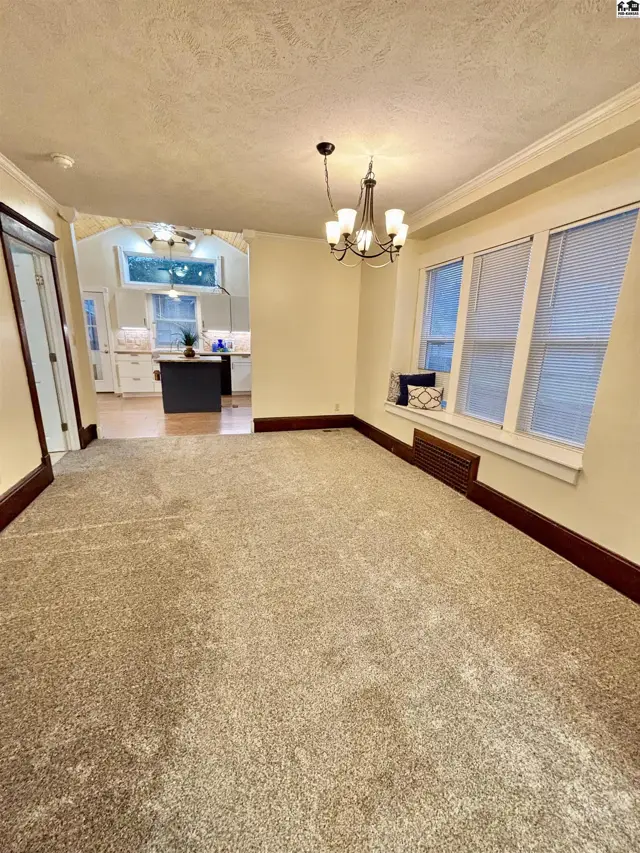 Spacious dining room with plush carpet, dark wood trim, and view into a modern kitchen.