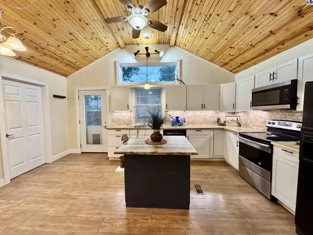Spacious kitchen with vaulted wood-paneled ceiling, white cabinets, granite countertops, and a central island.