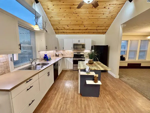 Spacious kitchen with vaulted wood ceiling, white cabinets, stainless steel appliances, and a central island.