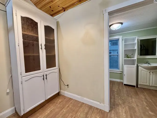 White built-in cabinet with glass doors and wood ceiling in a room with light wood floors.