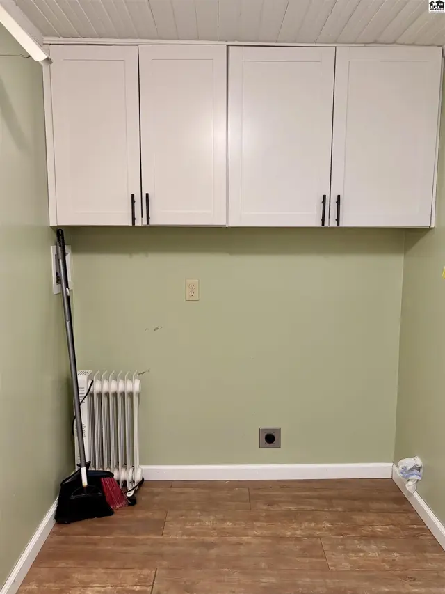 Laundry area with white upper cabinets, pale green walls, wood-look floor, and a radiator.