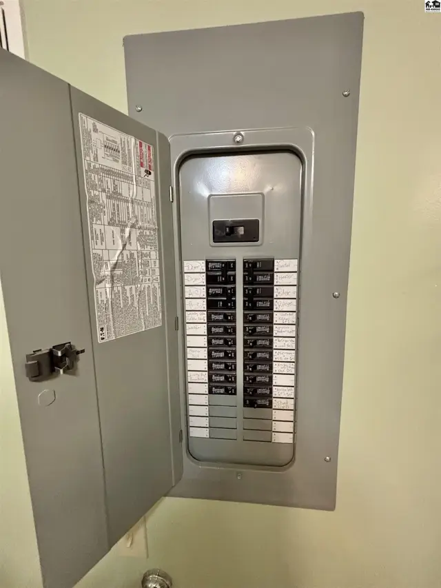 Gray metal electrical panel with breakers and a diagram on the open door.