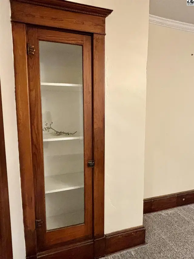 Tall, antique wooden display cabinet with glass door and white shelves against a cream wall.
