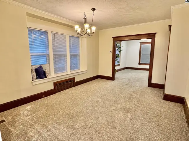 Spacious dining room with plush carpet, large bay window, and dark wood trim, opening to another room.
