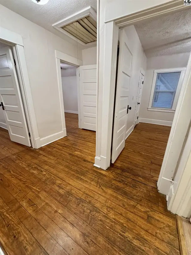 Hallway with warm, distressed hardwood floors, white paneled doors, and a pull-down attic access.