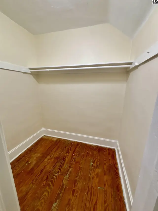 Empty closet with warm hardwood floors, white trim, and a single hanging rod.