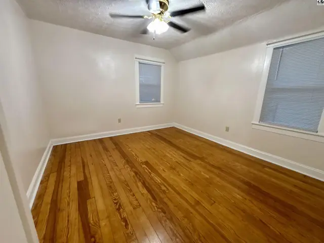 Bedroom with warm hardwood floors, white walls, and two windows.