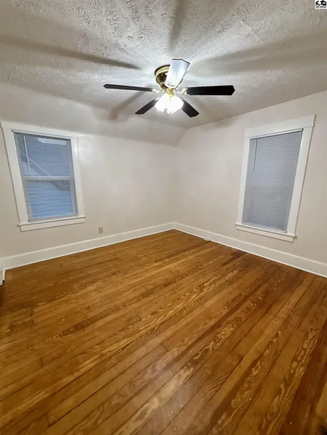 Bedroom with polished hardwood floors, two windows, and a ceiling fan.