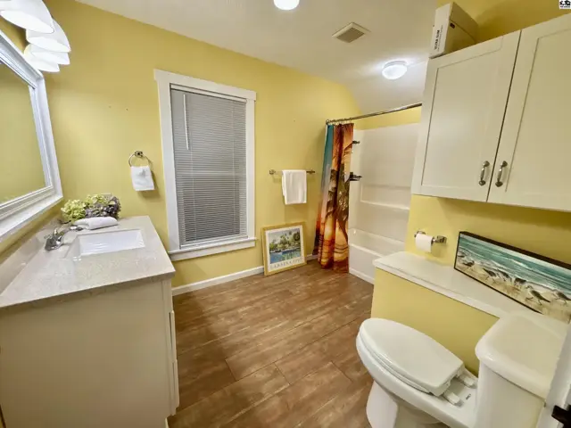 Bright yellow bathroom with a vanity, toilet, shower, and wood-look flooring.
