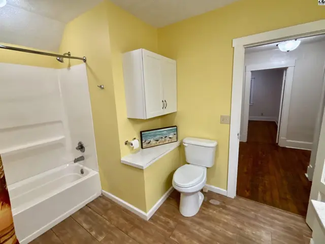 Bright yellow bathroom with white tub, toilet, vanity, and wood-look flooring.