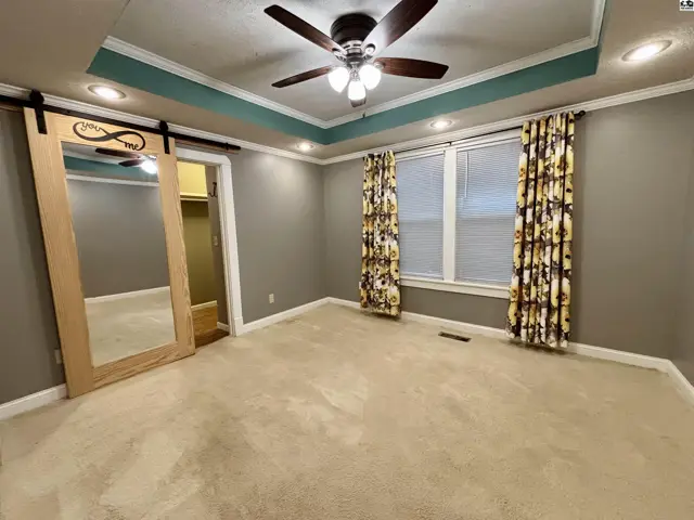 Spacious bedroom with tray ceiling, carpet, sliding barn door, and floral curtains.