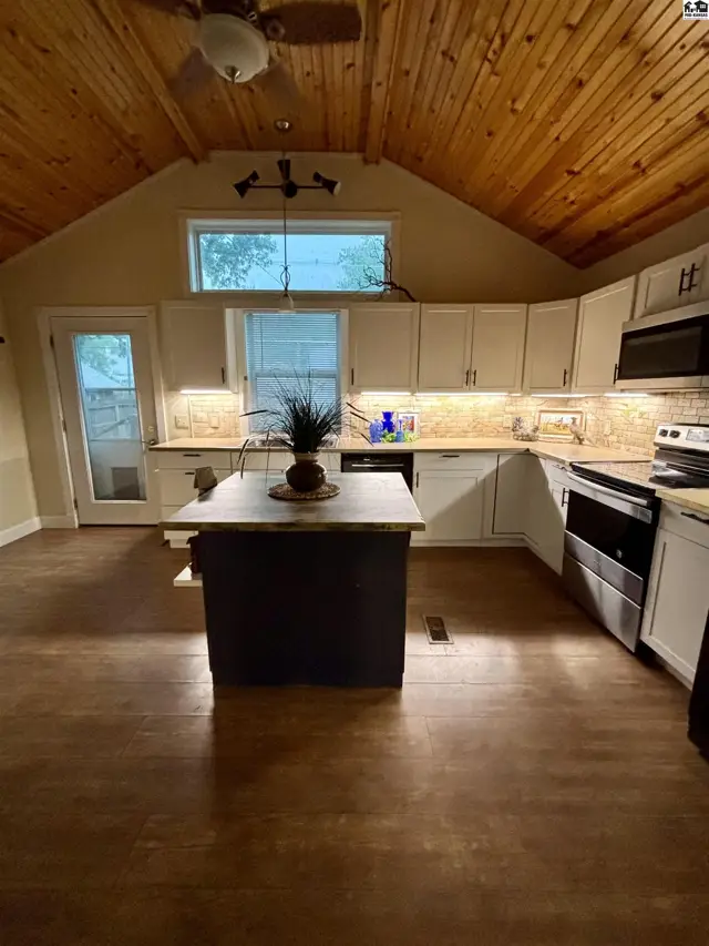 Spacious kitchen with vaulted wood ceiling, white cabinets, granite countertops, and a dark island.