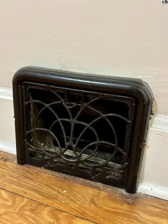 Ornate vintage cast iron floor vent with decorative scrollwork on hardwood floors.