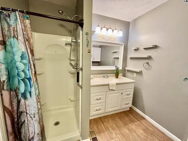 Bright bathroom with a white vanity, large mirror, and a white shower stall with a floral shower curtain.