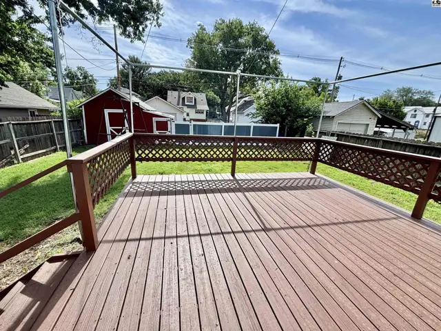 Spacious wooden deck with lattice railing overlooks a grassy yard and red shed.