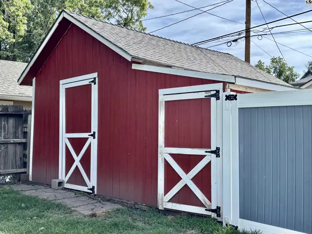 Red barn-style shed with white trim doors and a gray fence.