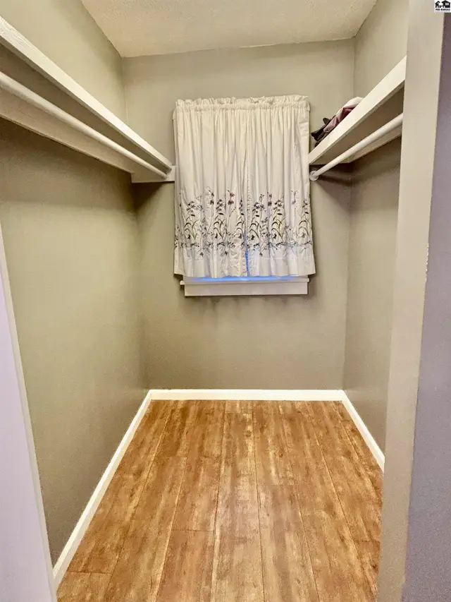 Spacious walk-in closet with light wood laminate flooring and built-in shelving.