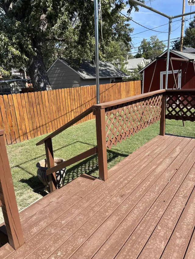 Wooden deck with lattice railing overlooks a fenced backyard with a shed.