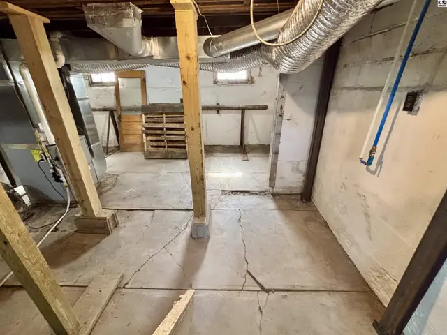 Concrete floor with visible cracks, exposed wooden beams, and ductwork in a basement.